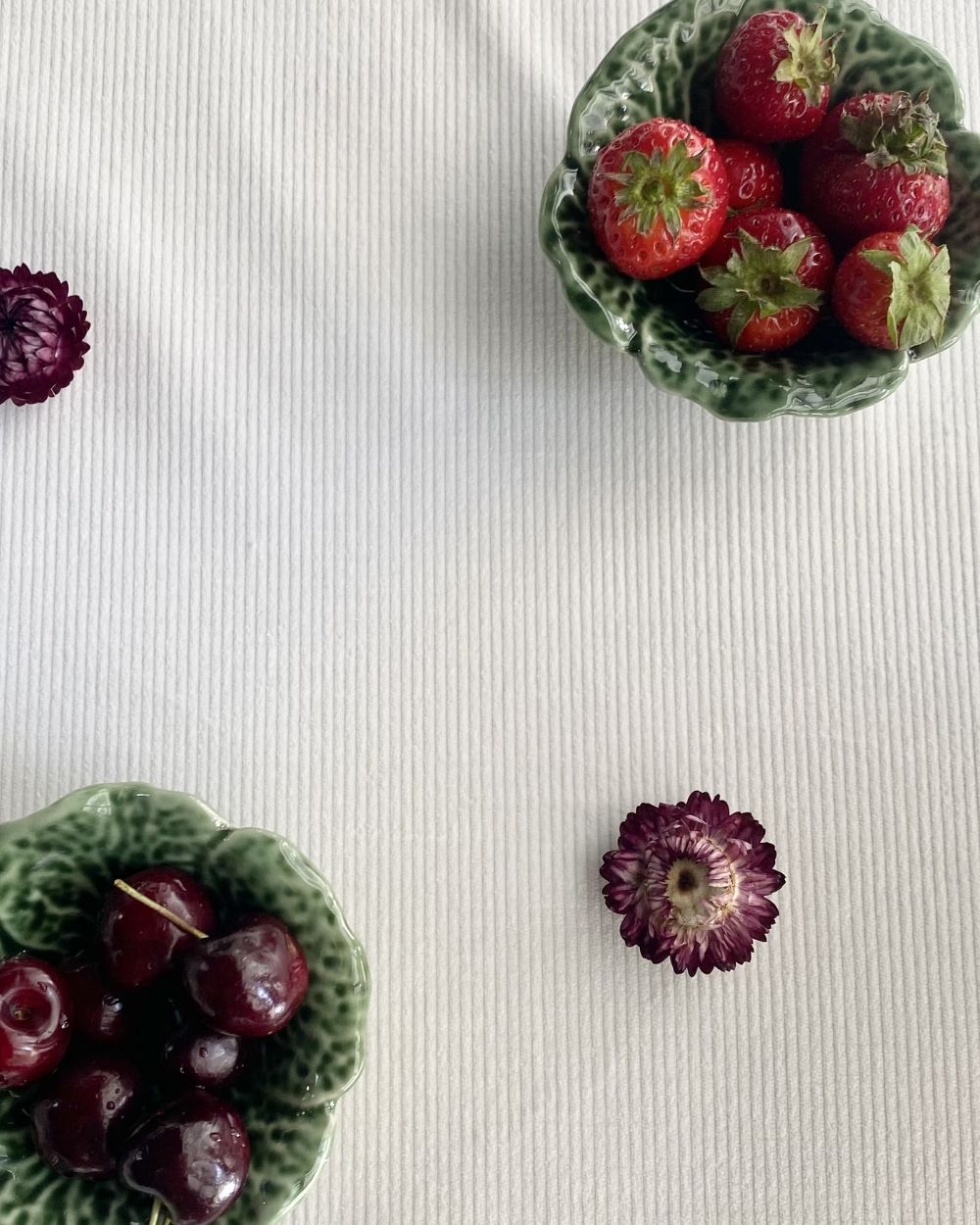 Bols de fraises et de cerises fraîches sur une nappe texturée, avec des fleurs séchées